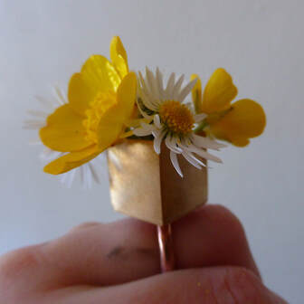 square copper ring containing daisy and buttercups on finger  