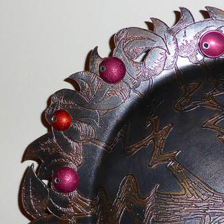 close up of dark shallow bowl with etched leaf detail and purple domed pieces