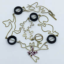 Roadkill Necklace, brass, rubber and garnet curled on white background